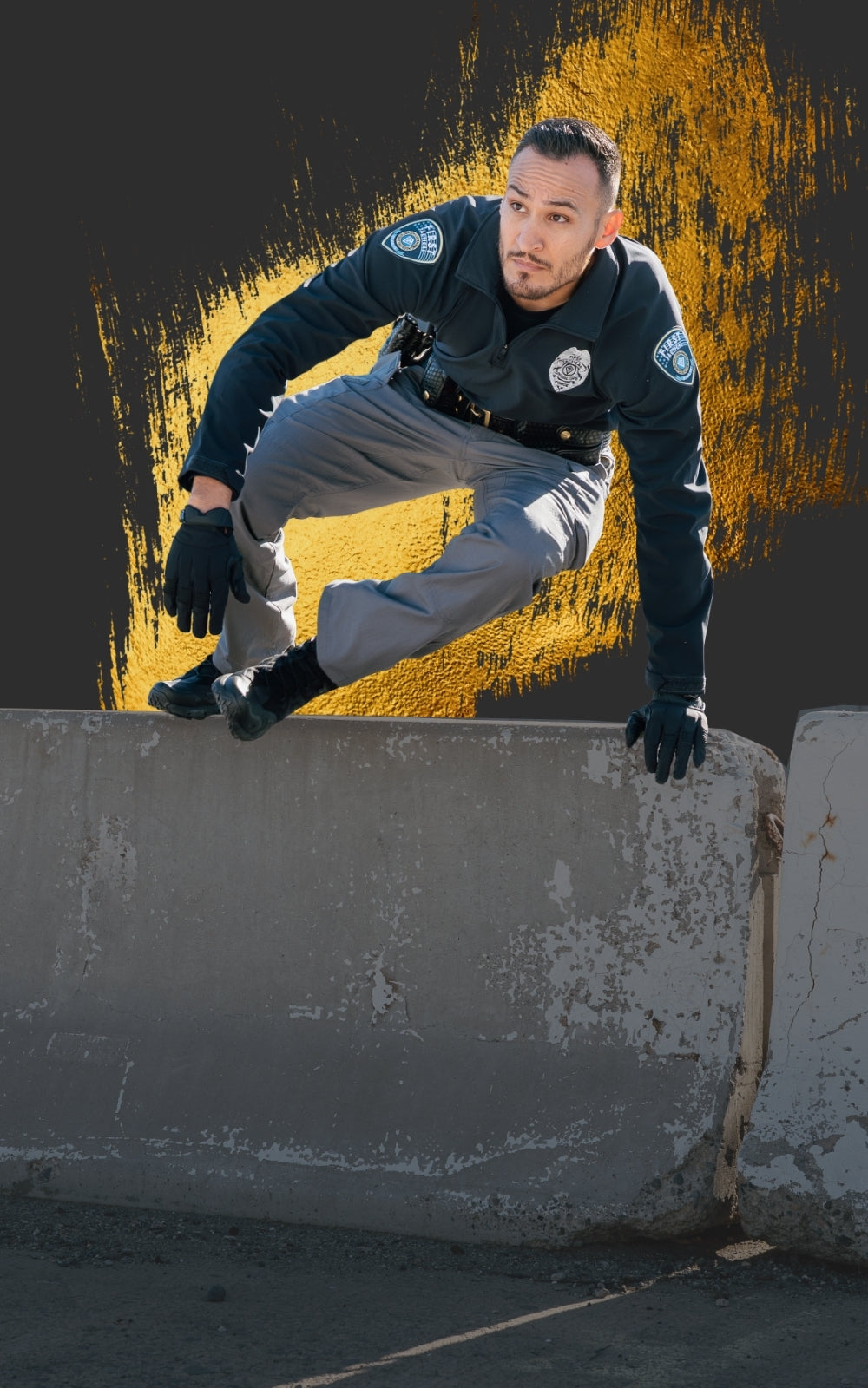 A man in a dark tactical uniform jumping over an concrete ledge against a dark gray background with a yellow paint-splatter graphic behind him. Text copy says "The V2 Tactical Pant. Better Equipped For Every Shift. Shop now"